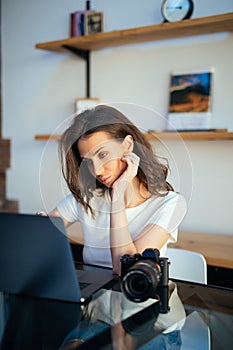 Freelance photographer woman with camera at home office editing photos on laptop