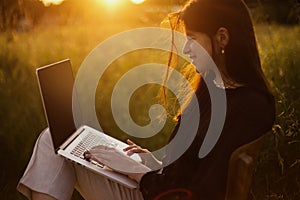 Freelance and remote work outdoors. Young business woman working online. Fashionable elegant girl with laptop sitting on rustic