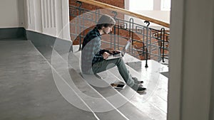 Freelance and technology. Handsome young man working on laptop computer sitting on stairs indoor in modern loft office.