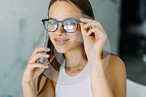 Freelance woman working from home, sitting at kitchen table, using laptop and having phone conversation, looking at computer