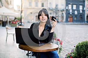 Freelance work concept. Young attractive Asian woman wearing black leather jacket, working on a laptop and drinking