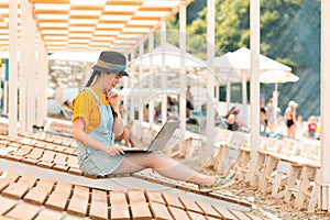 Freelance. A young woman sits on a sunbed and thoughtfully works at a laptop. Sun beds and umbrellas on the beach in the