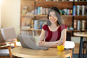 Freelancer Asian Girl Smiling At Camera While Working On Laptop In Cafe