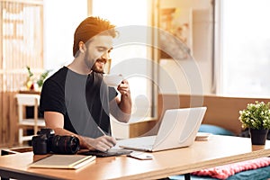 Freelancer bearded man drinking coffee at laptop sitting at desk.