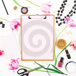 Freelancer or blogger workspace with clipboard, notebook, cosmetics, tulip flowers and accessories on white background. Flat lay,