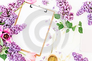 Freelancer or blogger workspace with clipboard, notebook, envelope, lilac, and tulips on white background. Flat lay, top view.