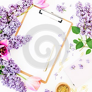 Freelancer or blogger workspace with clipboard, notebook, pen, lilac, and tulips on white background. Flat lay, top view.