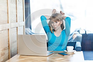 Freelancer with blonde hair in blue t-shirt are sitting in cafe and making video call on laptop, talking and teased with her