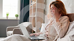Freelancer Caucasian woman working remote distant from home in bed thinking pensive holding head girl with laptop work