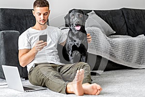 freelancer guy sitting at home working with a dog in an embrace, black labrador.