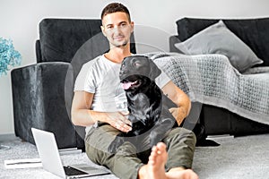 freelancer guy sitting at home working with a dog in an embrace, black labrador.