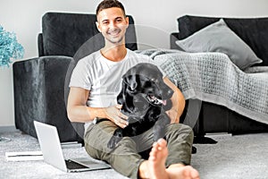 freelancer guy sitting at home working with a dog in an embrace, black labrador.