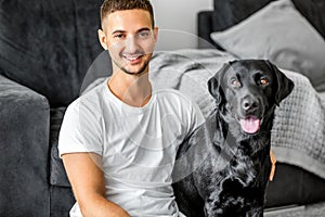 freelancer guy sitting at home working with a dog in an embrace, black labrador.