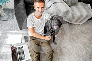 freelancer guy sitting at home working with a dog in an embrace, black labrador.