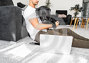 freelancer guy sitting at home working with a dog in an embrace, black labrador.