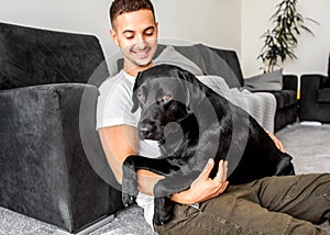 freelancer guy sitting at home working with a dog in an embrace, black labrador.