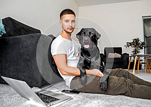 freelancer guy sitting at home working with a dog in an embrace, black labrador.