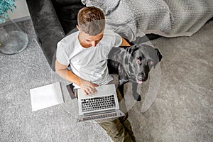 freelancer guy sitting at home working with a dog in an embrace, black labrador.