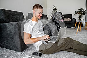 Freelancer guy sitting at home working in laptop and with dog in