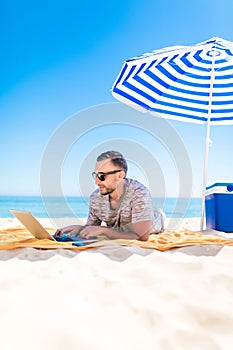 Freelancer, happy successful businessman in sunglasses on vocation with laptop on the beach under umbrella