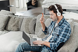 Freelancer in headphones having idea and using laptop on sofa