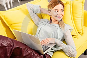 Freelancer lying on yellow sofa and using laptop at home