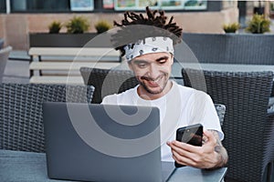 Freelancer male reading incoming notification on smartphone connected to 4G internet while working freelance at laptop. Hipster