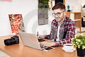 Freelancer man drawing on tablet at laptop sitting at desk.