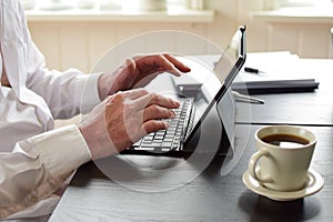 Freelancer man sits at a table and takes notes in a laptop.