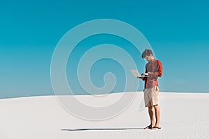 Freelancer on sandy beach with laptop against clear blue sky