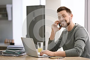 Freelancer talking on phone while using laptop at home