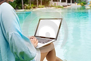 Freelancer using laptop working remotely near swimming pool. Young Asian traveler woman working on computer during her summer