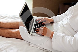 a freelancer on vacation works at a laptop lying on a bed in a white coat. Close-up, no face. A man& x27;s hands on a