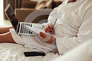 a freelancer on vacation works at a laptop lying on a bed in a white coat. Close-up, no face. A man& x27;s hands on a