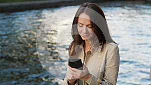 Freelancer woman browsing in smartphone, sitting against river water.