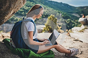 Freelancer woman with glasses and headphones uses digital tablet device working in summer nature outdoor, tourist girl