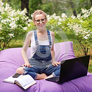 Freelancer working in the garden. Writing, surfing in the internet. Young woman relaxing and having fun in park area drinking