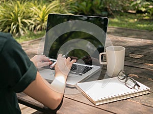 Freelancer working on laptop computer with white coffee cup on the wooden desk in the garden