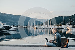 Freelancer working on laptop on the shore near the yacht boat at