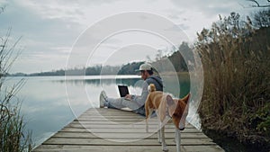 Freelancer works on his laptop outdoor next to lake, sitting on pond