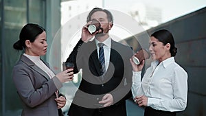 Freelancers colleagues drinking coffee in business clothes standing outdoors near office building. Business people