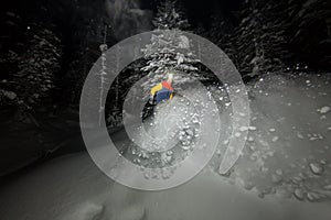Freerider snowboarder jumping at night with a springboard in the forest