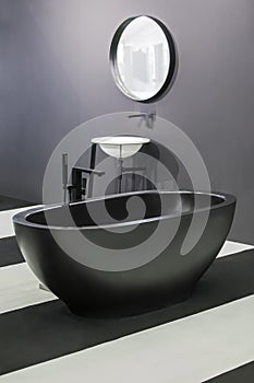 Freestanding black bathtub, stylish minimalist black and white loft style bathroom. Bath, washstand, mirror on the wall