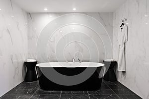 Freestanding black bathtub, stylish minimalist black and white loft style bathroom. Bath, washstand, walls with marble