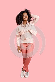 Freestyle. African girl in denim jacket standing isolated on pink touching hair posing to camera joyful