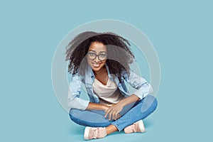 Freestyle. African girl in glasses sitting isolated on gray leaning forward smiling happy