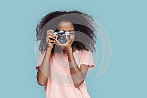 Freestyle. African girl standing isolated on gray taking photo with film camera smiling cheerful
