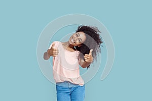 Freestyle. African girl standing isolated on gray tilting head thumbs up smiling happy