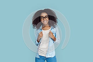 Freestyle. African girl wearing glasses standing  on gray posing in jeans jacket smiling cheerful