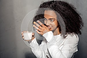 Freestyle. African girl in white outfit standing isolated on gray wiping off milk from lips laughing playful close-up